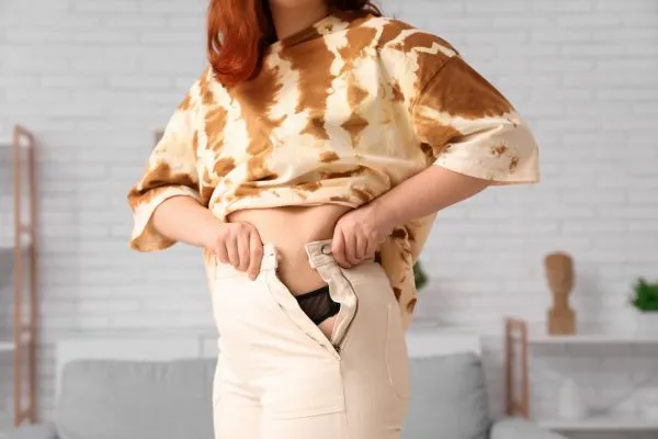 Image of woman trying to do her trousers up after pregnancy weight gain Wisbech